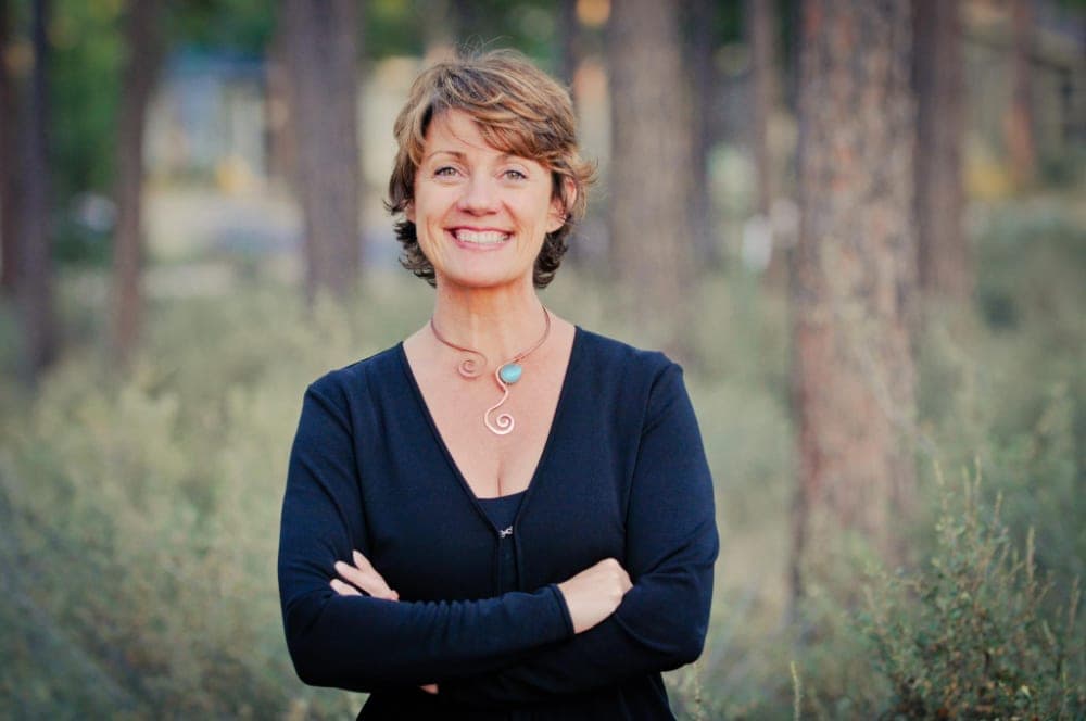 Angela Freeman smiling outdoors among pine trees