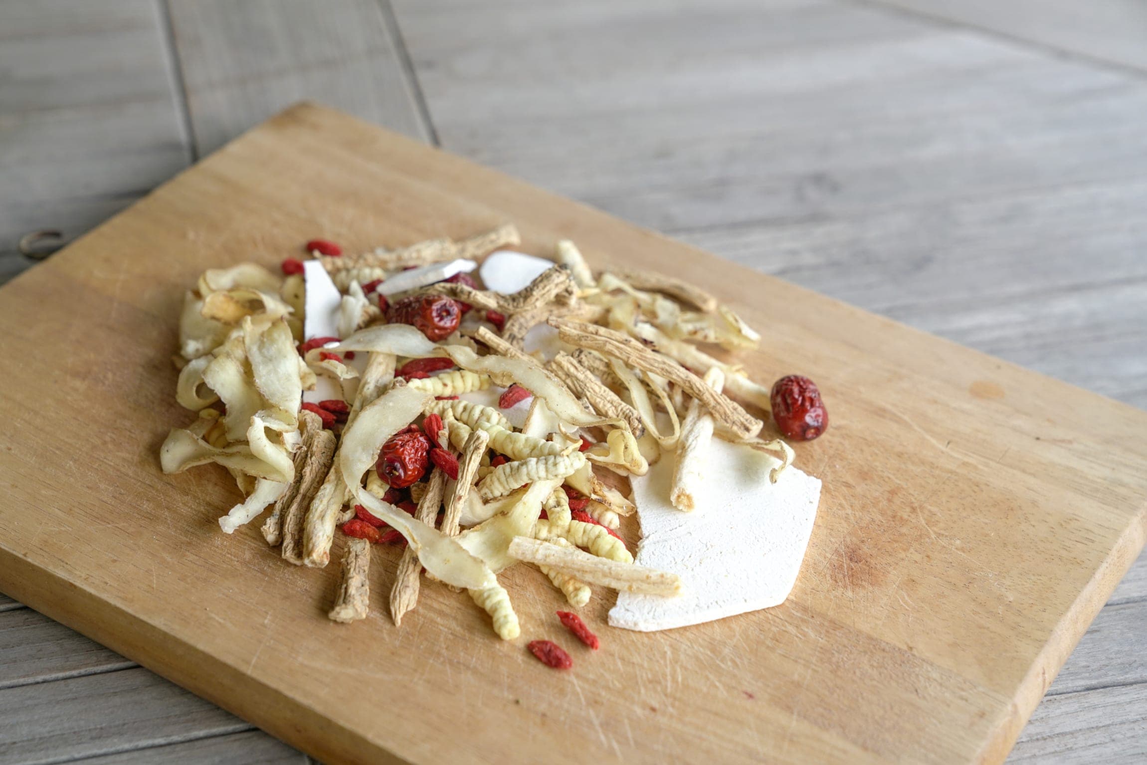 Dried Chinese herbs, goji berries, and root slices on a wooden cutting board