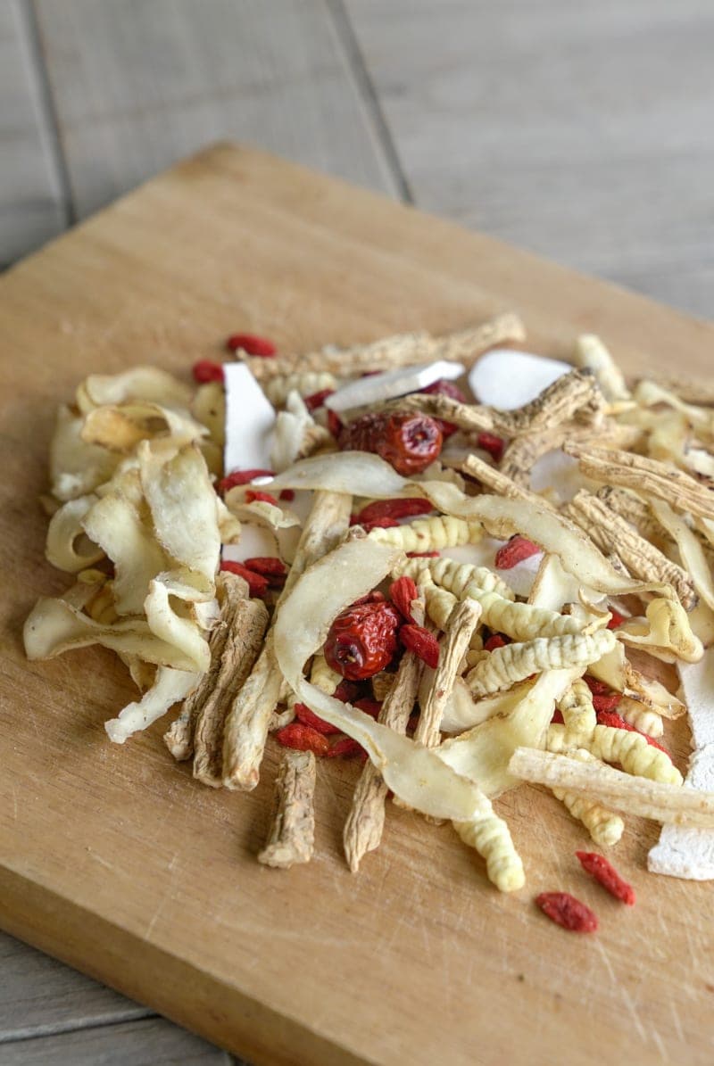 A mix of dried Chinese herbs, goji berries, and root slices spread on a wooden cutting board